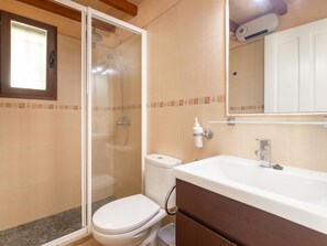 Une salle de bain avec une douche à parois de verre, des toilettes blanches et un grand lavabo blanc avec un miroir au-dessus.