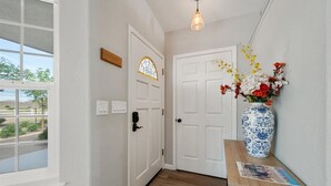 A hallway with a wooden floor, a white door with a stained glass window, a vase with flowers, and a hanging light fixture. - Newly remodeled 4-bedroom, 3-bathroom home with jacuzzi close to downtown Paso (Paso Robles)
