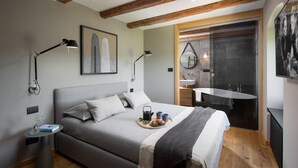 A modern bedroom with a large bed, bedside lamps, a painting, a bathroom with a sink and bathtub, and wooden beams on the ceiling. - Cozy home in Labin with WiFi (Labin)