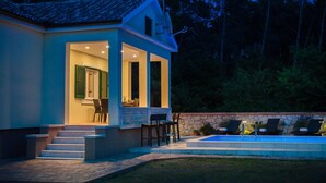 Una casa moderna con piscina, mobiliario de exterior e ingreso bien iluminado.