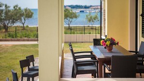 Un patio con mobiliario de mimbre, una mesa con un florero y vistas al mar y árboles.