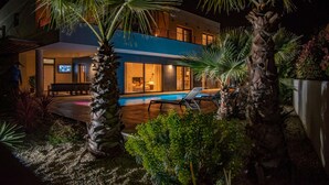 Ett modernt hus med en swimmingpool, palmer och en balkong med utsikt över poolen.