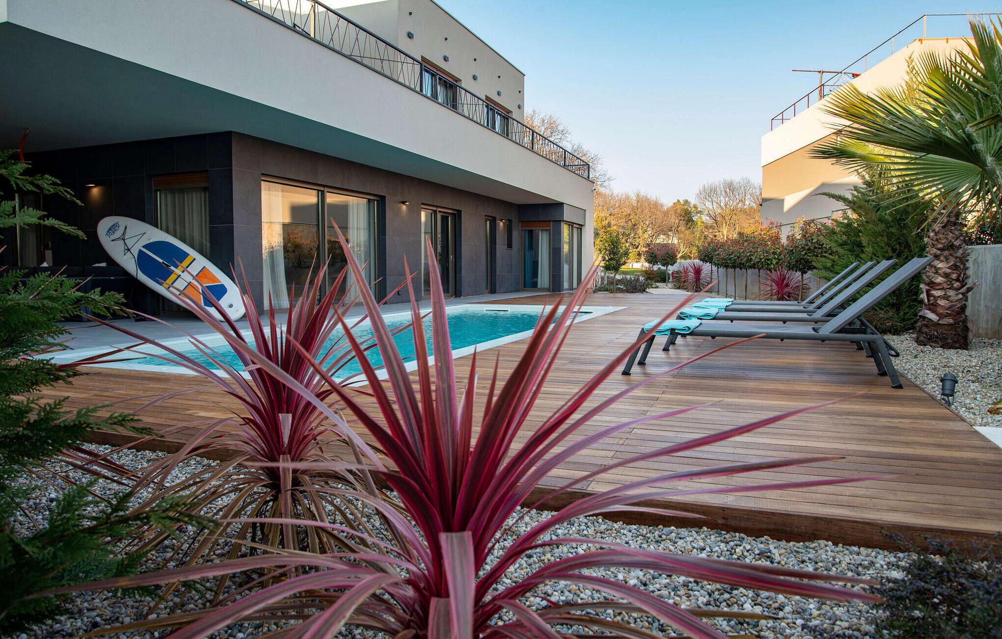 Une maison moderne dotée d’une piscine, d’une terrasse en bois et de chaises longues.