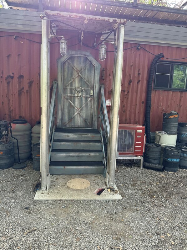 A metal staircase leading to a door with a lock, surrounded by storage tanks and a red utility box.