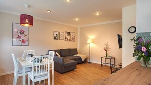A modern living room with a dining area, a grey sofa, a wooden dining table with chairs, a red pendant light, and a wall-mounted TV. - Ferienwohnung Rosengasse 3, bis 4 Personen, 50qm, Terrasse (Bad Reichenhall)
