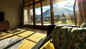 A room with large windows, a wooden floor, a sofa, and a TV.