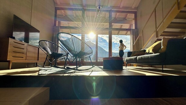 A spacious living room with a large window, a sofa, a chair, and a wooden cabinet.