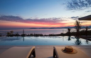 An infinity pool with a sunset view, lounge chairs, and a straw hat on the edge. - Villa Brilliance House (Orebic)