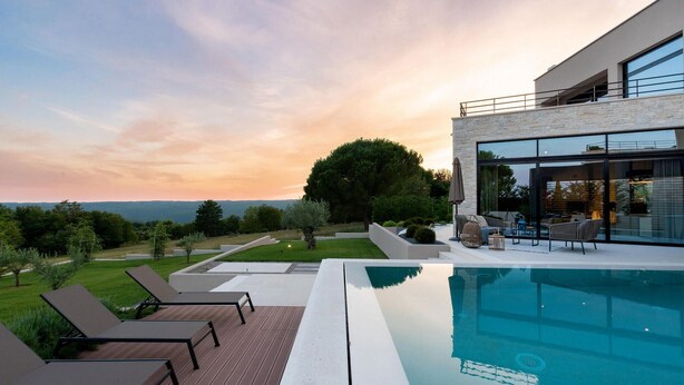 Un área de piscina moderna al aire libre con sillones de descanso, un porche con paredes de cristal y vistas al paisaje.