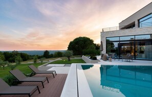Ein moderner Poolbereich im Freien mit Liegestühlen, einer gläsernen Veranda und Blick auf die Landschaft.
