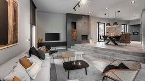 Una sala de estar moderna con sofá, mesa de centro y televisor. Una escalera conduce a un comedor con sillas y mesa.