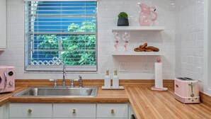 Eine Küche mit Spüle, Holz Arbeitsplatte, weißen Schränken, einem Fenster mit Jalousien und einem rosa Toaster.