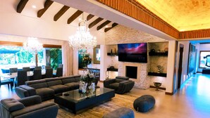 A spacious living room with a large sectional sofa, a coffee table, and a fireplace. There is a flat-screen TV mounted above the fireplace and a chandelier hanging from the ceiling. - Llano Grande (Rionegro)