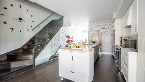 Cocina moderna con escalera de madera, un armario blanco y un frutero, y un reloj de pared.