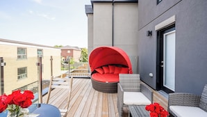 Una terraza con mobiliario de mimbre, una silla roja y una mesa con rosas rojas.