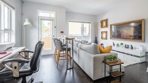 Una sala de estar moderna con un sofá gris, sillas de cuero negro, una mesa de comedor de madera y un cuadro grande enmarcado en la pared.