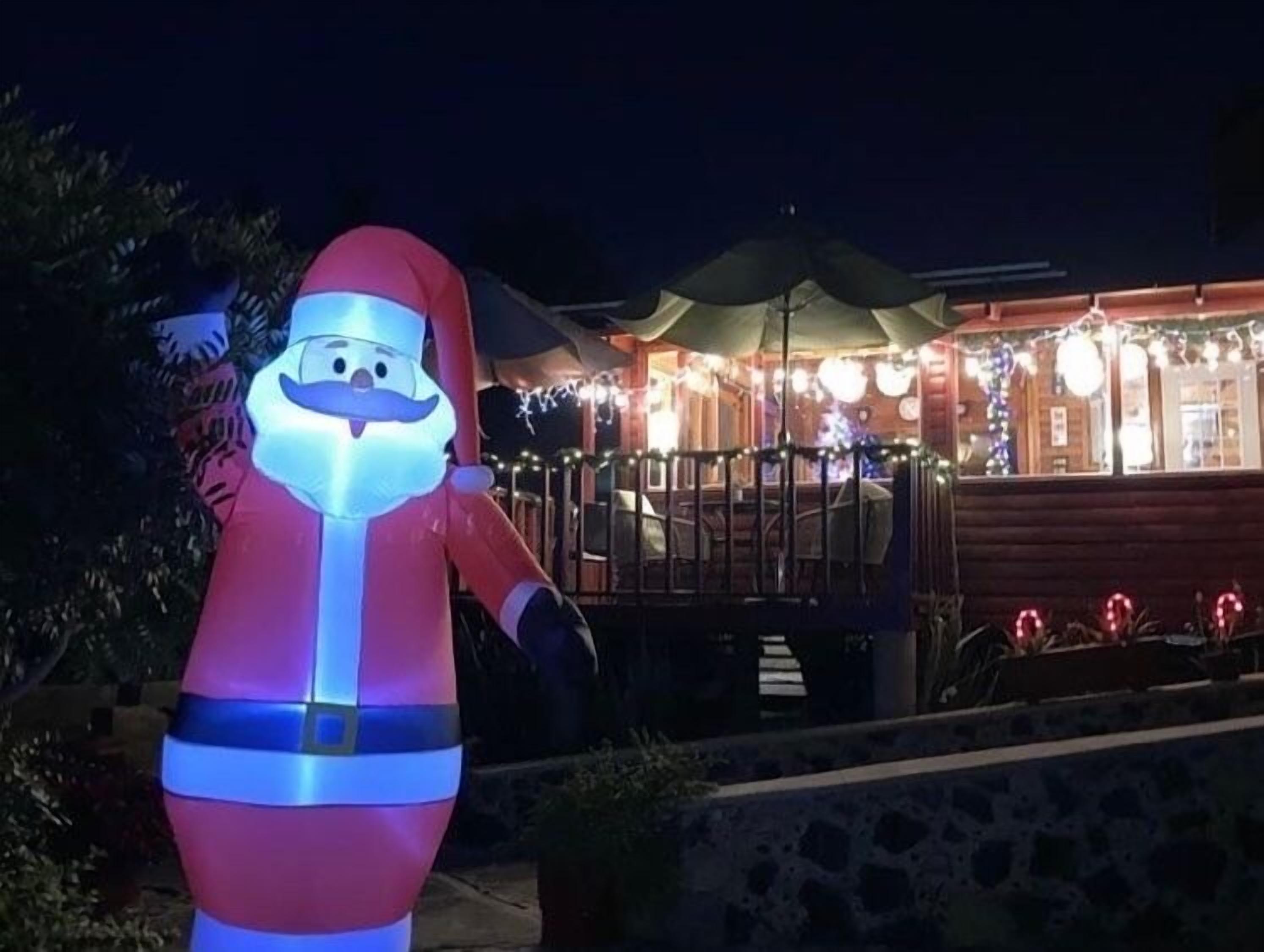 A large illuminated Santa Claus figure outside a building with a wooden facade and string lights.