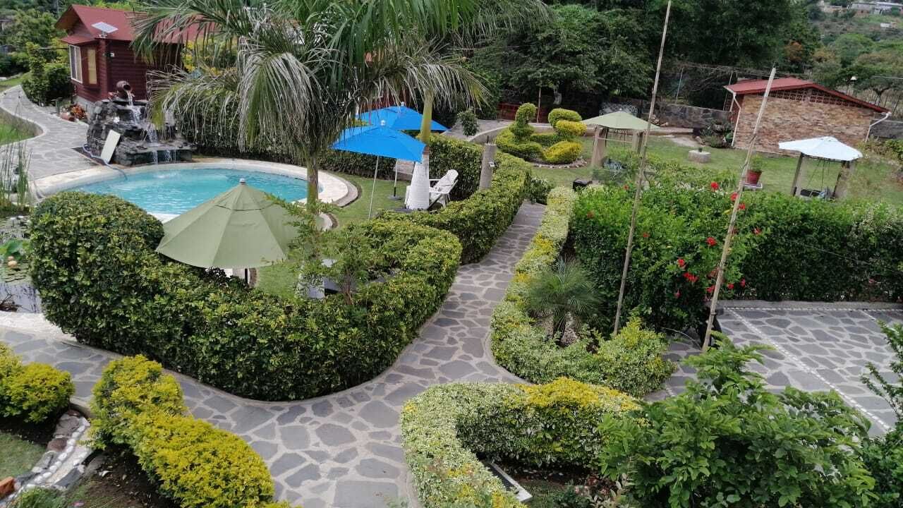Una zona enjardinada amb una piscina, senders de pedra i diferents elements decoratius de jardí.