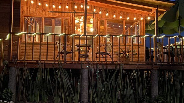 Una cabaña de madera con un porche, luces colgantes y asientos al aire libre.