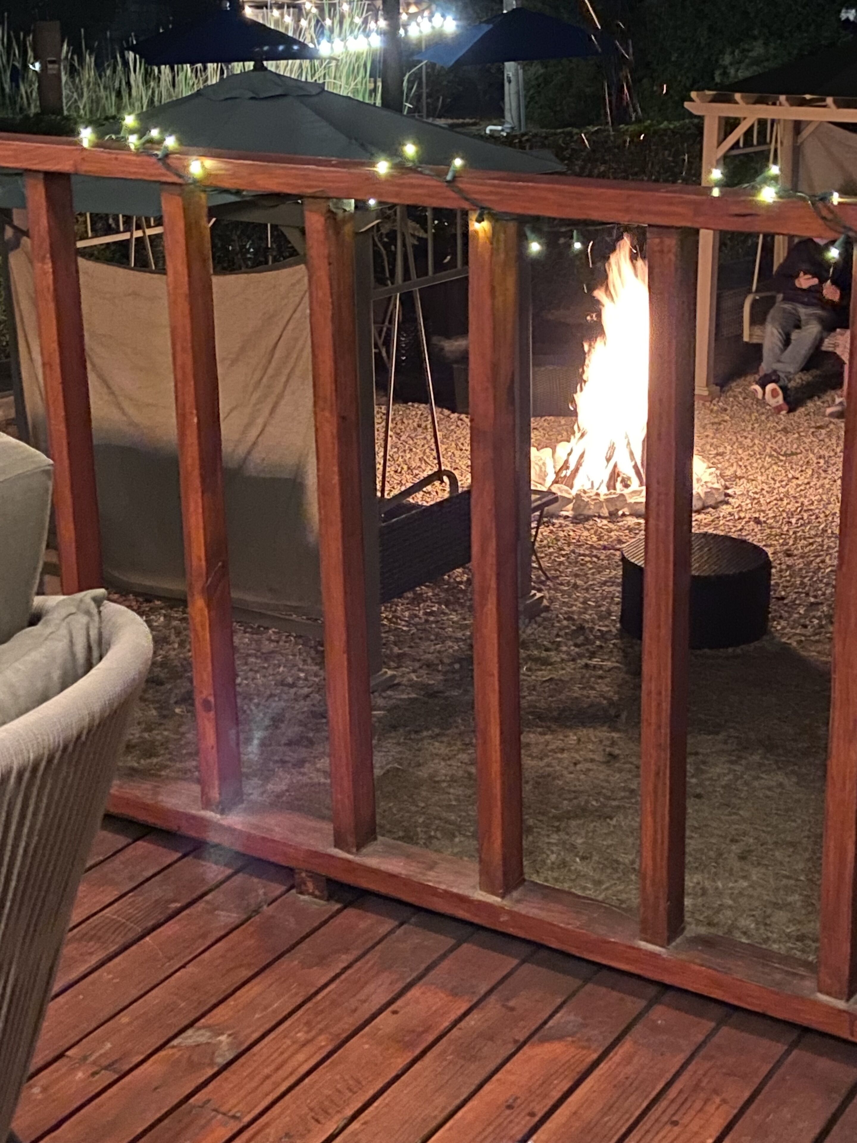 Una terraza de madera con un brasero y luces colgantes.