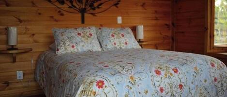A wooden cabin bedroom with a bed, two bedside lamps, and a wall-mounted decorative piece.