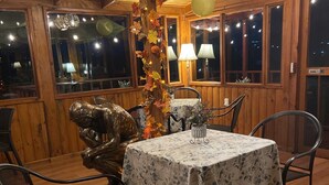 Un interior de madera con una mesa redonda cubierta por un mantel floral, rodeada de sillas de metal.