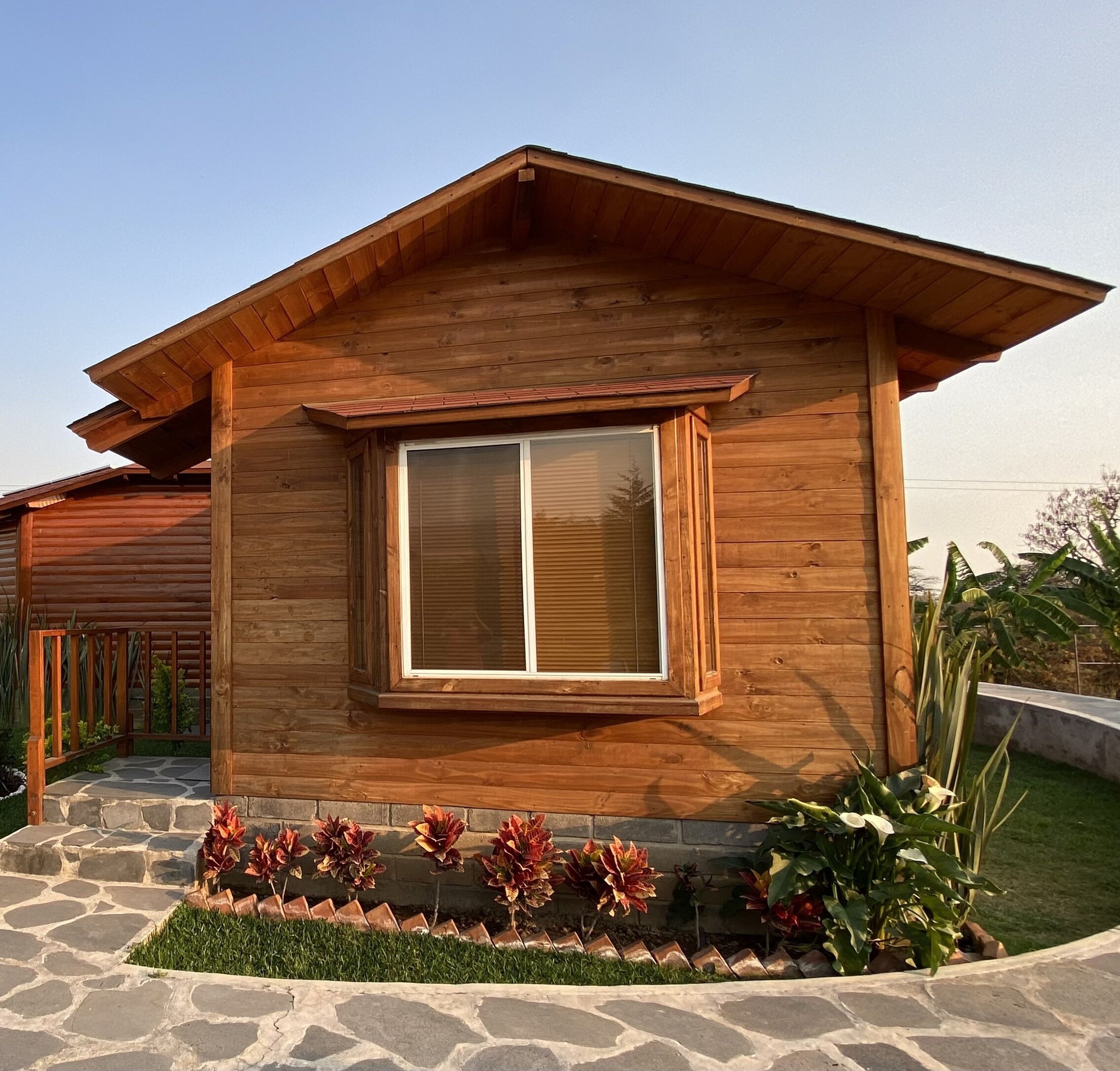 A wooden house with a large window, stone pathway, and a small garden with plants.