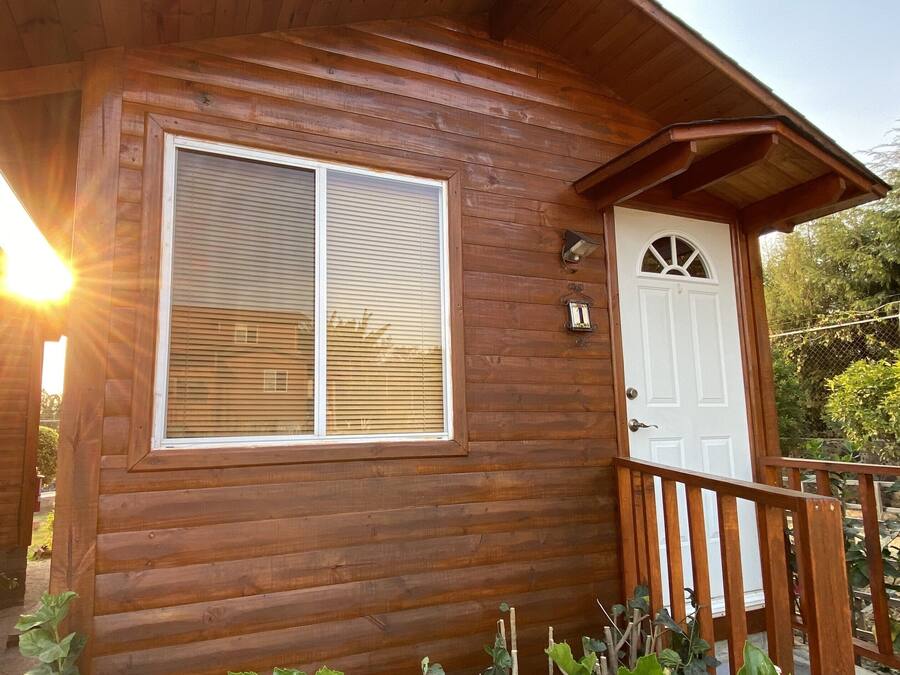 A wooden cabin with a large window, a door, and a small porch with a railing.