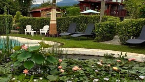 Un jardín tranquilo con un estanque, lirios acuáticos blancos y rosados, y un edificio rojo con balcón.