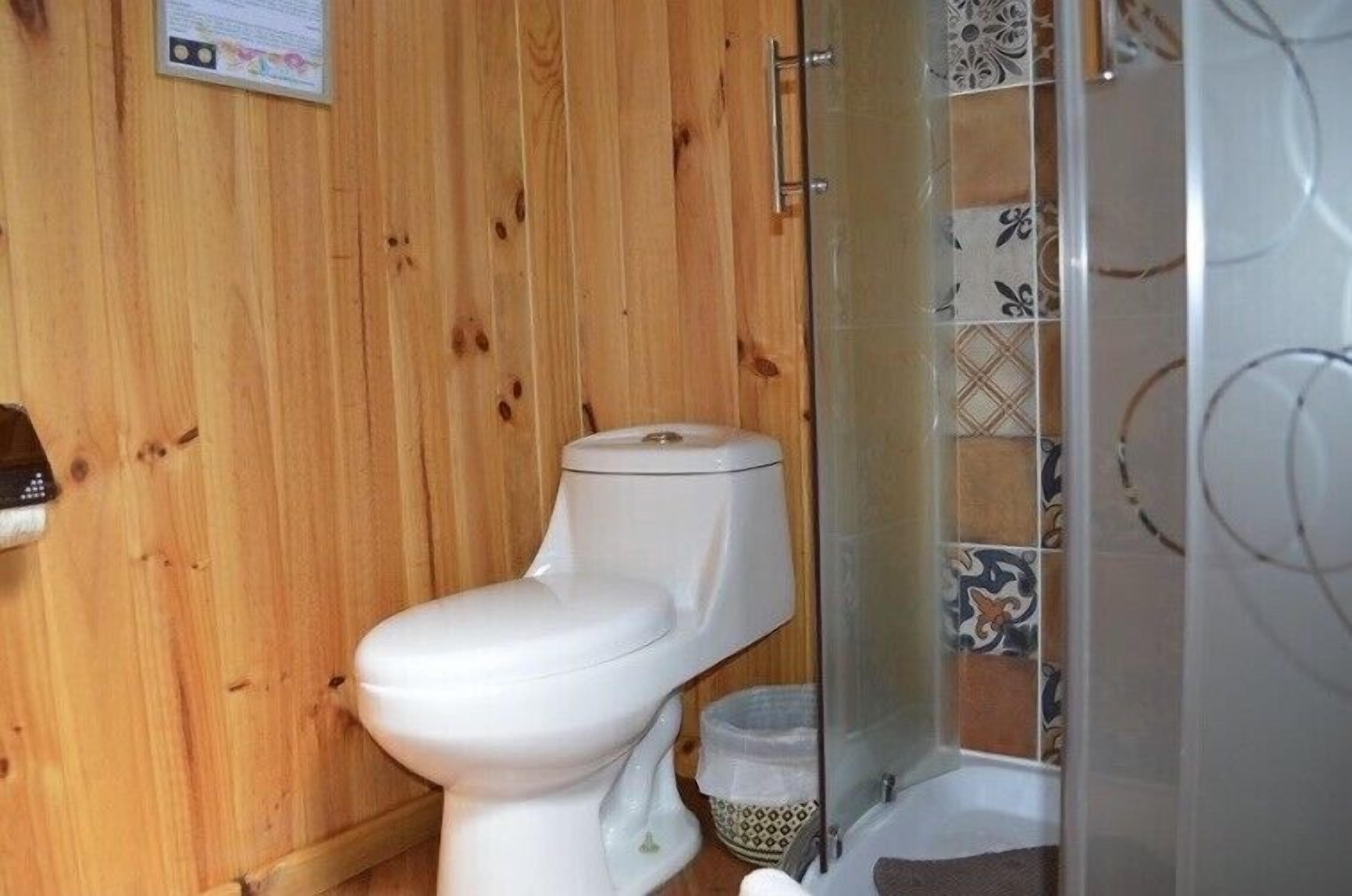 Un baño con paneles de madera, un inodoro blanco, cabina de ducha y zona de ducha azulejada.