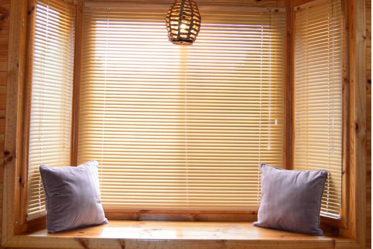 A wooden cabin with a bench seat and two pillows, a hanging light fixture, and wooden blinds.