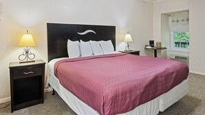 Habitación de hotel con una cama grande, dos mesitas de noche con lámparas, un ventilador de techo, una ventana con vistas y una pequeña mesa con cafetera.