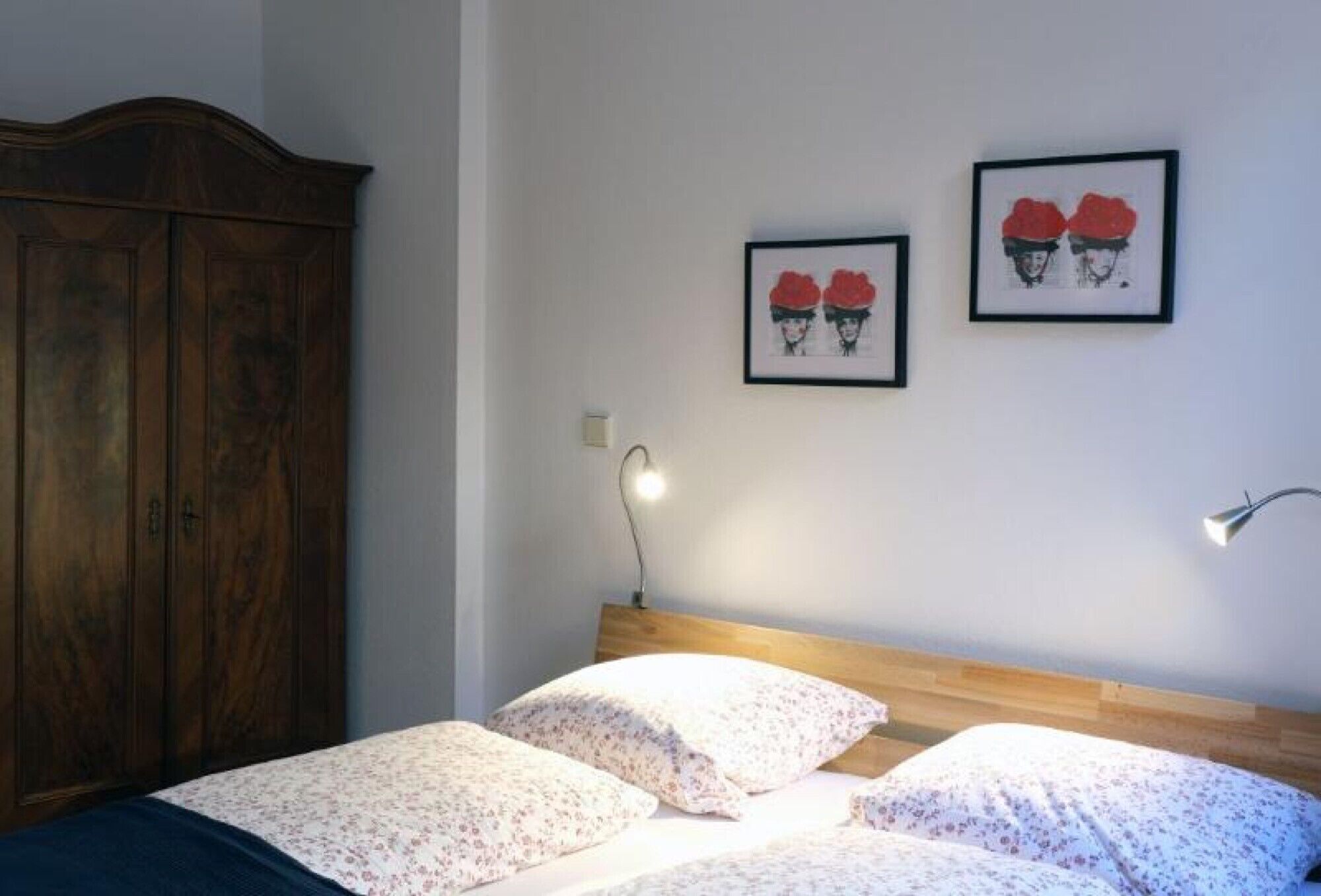 Un dormitorio con cabecera de madera, una cama con ropa de cama floral, dos cuadros en la pared y una mesita de noche con una lámpara.