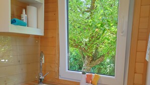 Eine Küche mit Spüle aus Edelstahl, Holzschränken, einem Fenster mit Blick auf Grünflächen und einer Arbeitsfläche mit Schneidebrett und Messer.