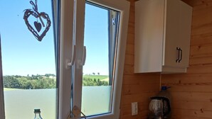 Une cuisine avec des meubles de rangement en bois, une fenêtre décorée d’un motif en forme de cœur, une bouteille d’eau et une bouilloire.