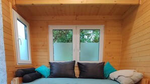 Une petite cabane en bois avec un lit, une fenêtre et une paire de chaussons posés sur un tapis.