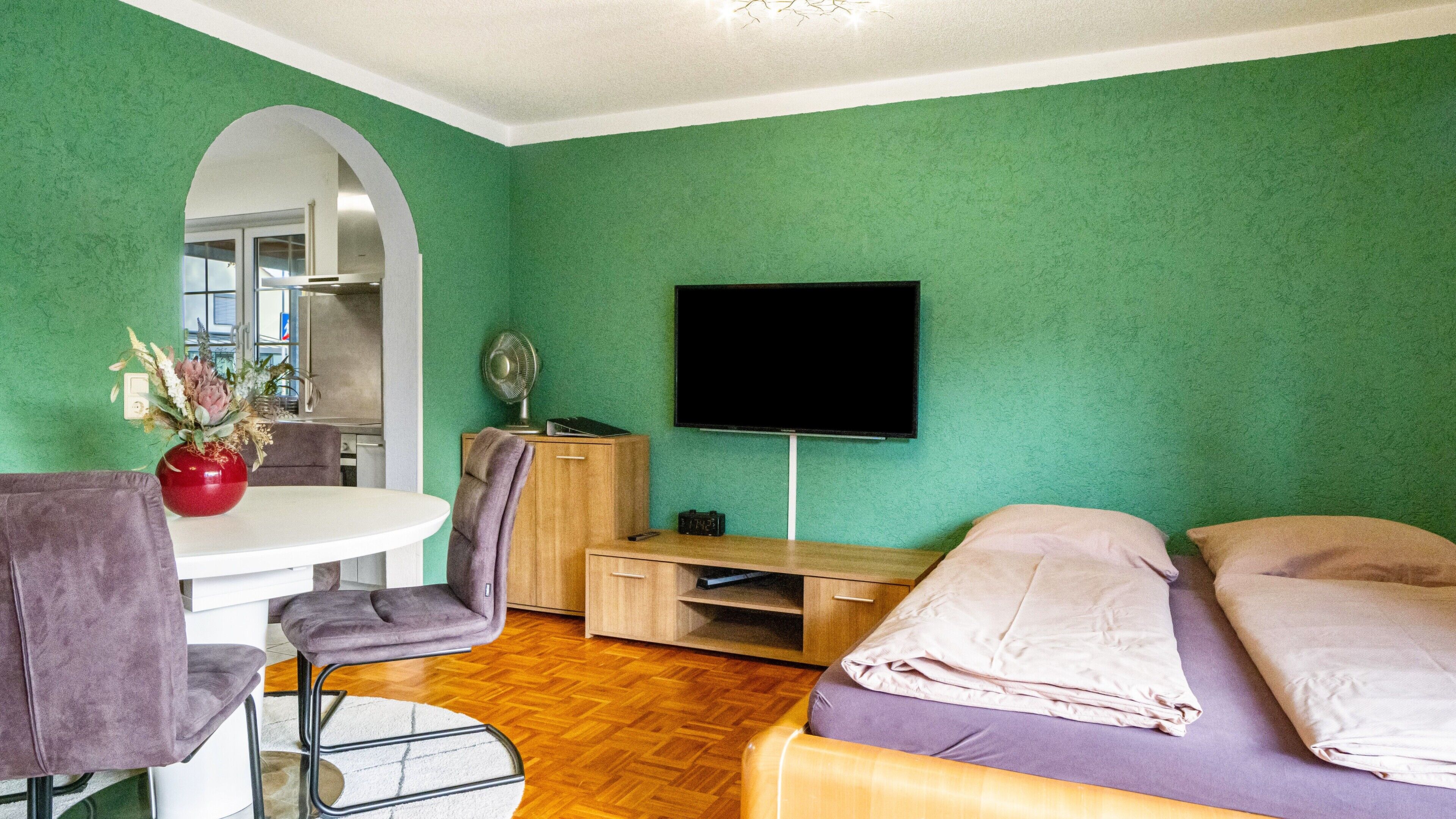 A room with a bed, a desk, a chair, a TV, and a dining table.