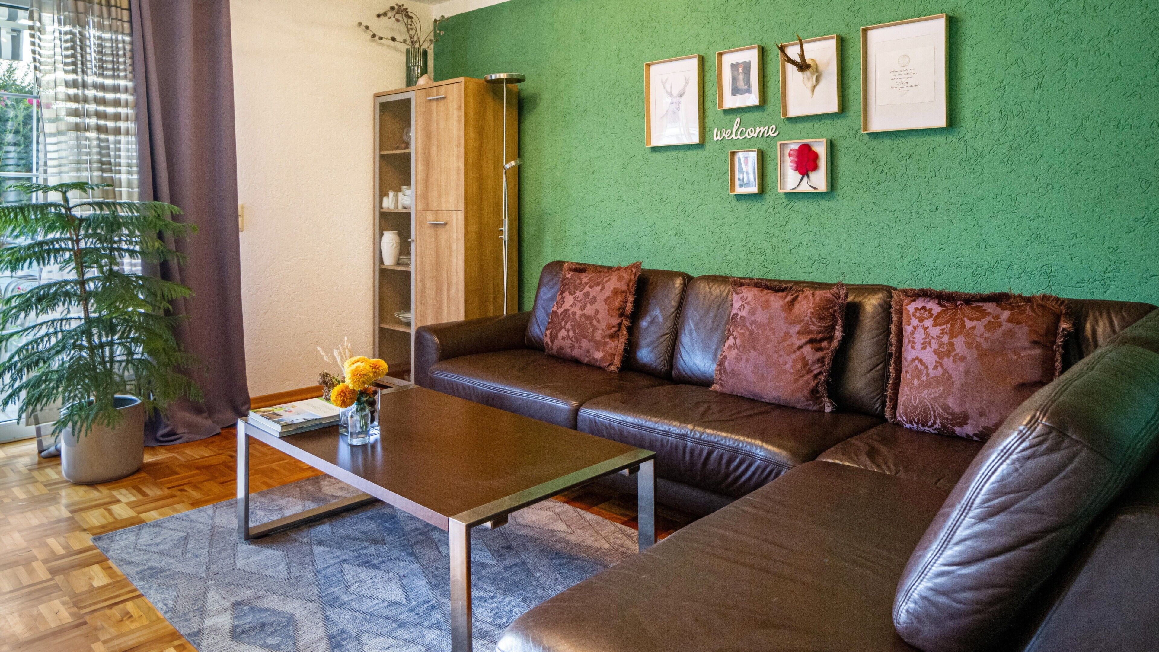 Una sala de estar con un sofá de cuero marrón, una mesa de centro, una pared verde con cuadros enmarcados y un mueble de madera.