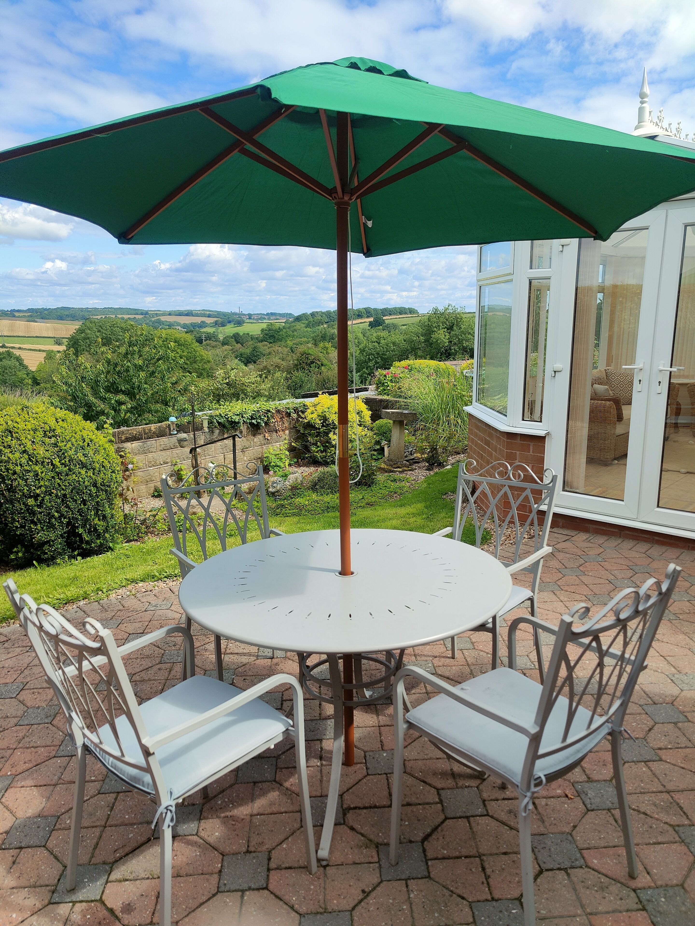 A round patio table with four white chairs and a green umbrella.