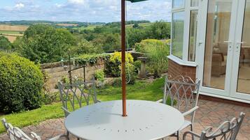 A round patio table with four white chairs and a green umbrella.