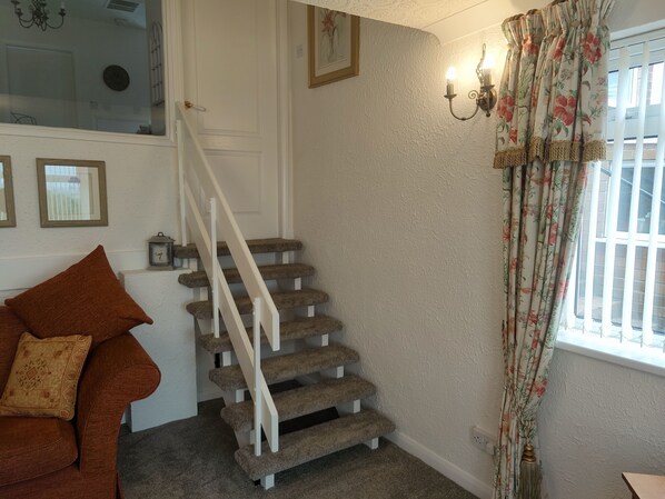 A staircase with carpeted steps and white railings, a floral curtain, and a brown sofa with a patterned cushion. - Split Level Bungalow - Sleeps4 - Close to walks (Sutton-in-Ashfield)
