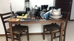 Une table à manger avec des chaises, des appareils de cuisine, ainsi que divers plats et ustensiles.