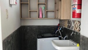Une cuisine de taille réduite équipée d’un lave-linge, d’un évier et d’un extincteur.