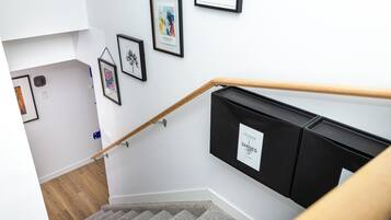 Un escalier avec une rampe en bois, un meuble noir pour ranger les chaussures et des tableaux encadrés accrochés au mur.