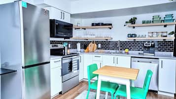 Une cuisine moderne avec des appareils en acier inoxydable, des chaises vertes et une table en bois.