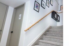 Een trap met een houten leuning, een deur met een bordje en lijstwerken aan de muur.