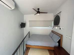 Ein kleines Zimmer mit einem Einzelbett, Deckenventilator, Wandfernseher und einem Nachttisch.