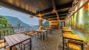 Un restaurant avec des tables et des bancs en bois, une fresque représentant un paysage tropical et une vue sur les montagnes.