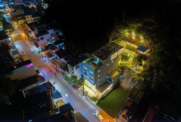 Ein Luftbild einer beleuchteten Stadt bei Nacht mit Gebäuden, einer Hauptstraße und einem Hügel mit einer erleuchteten Struktur.