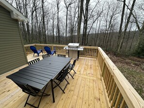 A wooden deck with a table and chairs, a grill, and a view of a forest. - Secluded mountain home on over 10 wooded acres, modern, WiFi and pet friendly! (Westfield)